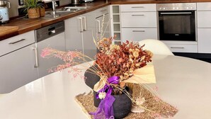 A modern kitchen with stainless steel appliances, a dining table with a vase of dried flowers, and pendant lighting. - Far-reaching views of the Mangfall valley - Quiet house with sauna, hot tub & garden near Munich (Feldkirchen-Westerham)