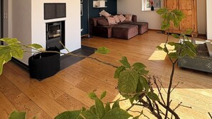 A spacious living area with a fireplace, dark walls, wooden flooring, and a large window. - Far-reaching views of the Mangfall valley - Quiet house with sauna, hot tub & garden near Munich (Feldkirchen-Westerham)