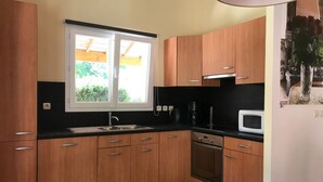 Cocina compacta con armarios de madera, encimera negra, ventana con vistas a zonas verdes, horno empotrado y microondas.