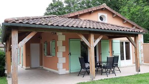 Un espacio al aire libre techado con mesa y sillas de patio, un pequeño horno de ladrillo y una puerta con ventanal.