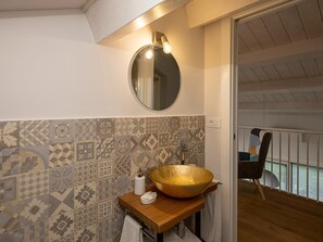 A bathroom with a wooden vanity, a large gold bowl sink, patterned tiles, a round mirror, and a ceiling light fixture. - Spacious Stay in Montelupone (Montelupone)