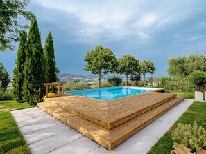 Ein rechteckiger Pool mit Holzterrasse, umgeben von Grün und Blick auf ferne Hügel.