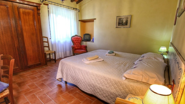 Ein Schlafzimmer mit Bett, Sessel, Fernseher und Lampe.