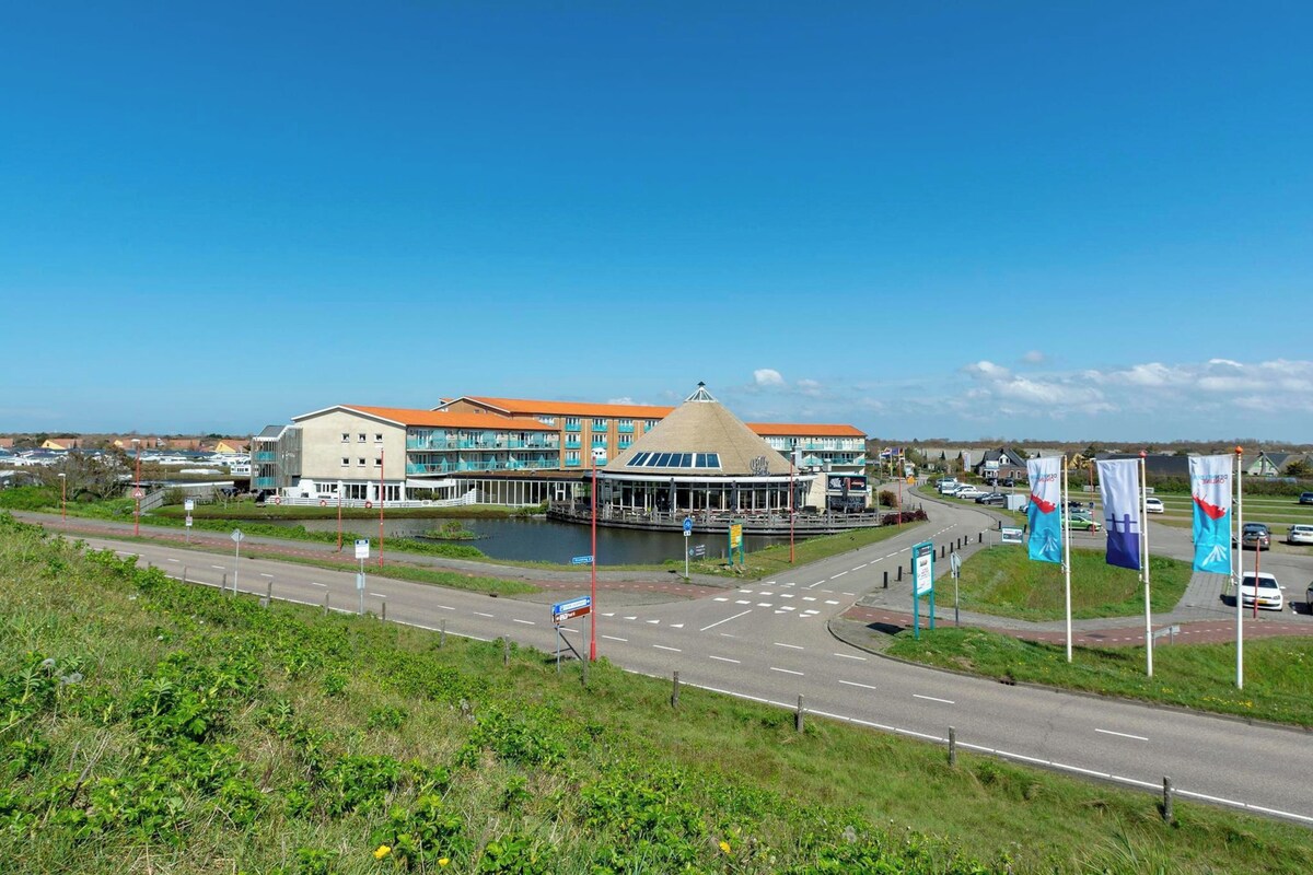 A modern building with a unique architectural design, a waterfront, and a road leading to it.
