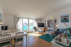 A bright living room with a dining area, a sofa, a bookshelf, and a television. - Bright Coastal Hideaway (Julianadorp)