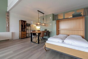 A bedroom with a bed, a desk with chairs, a wooden cabinet, and a hanging light fixture. - Bright Coastal Hideaway (Julianadorp)