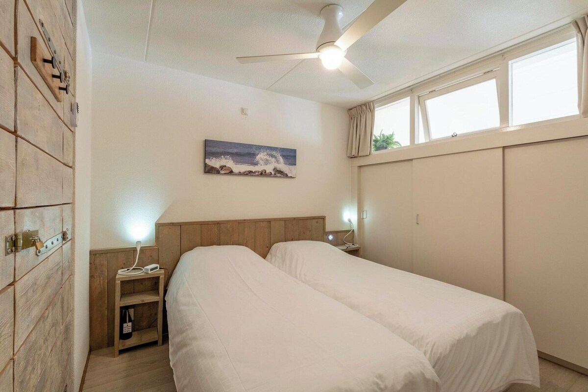 A bedroom with two beds, a ceiling fan, a painting, and a window with curtains.