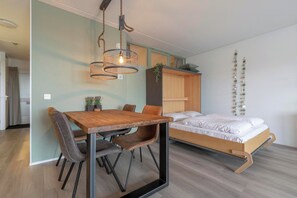 A modern room with a wooden dining table, chairs, a bed with a wooden frame, and a hanging light fixture. - Bright Coastal Hideaway (Julianadorp)