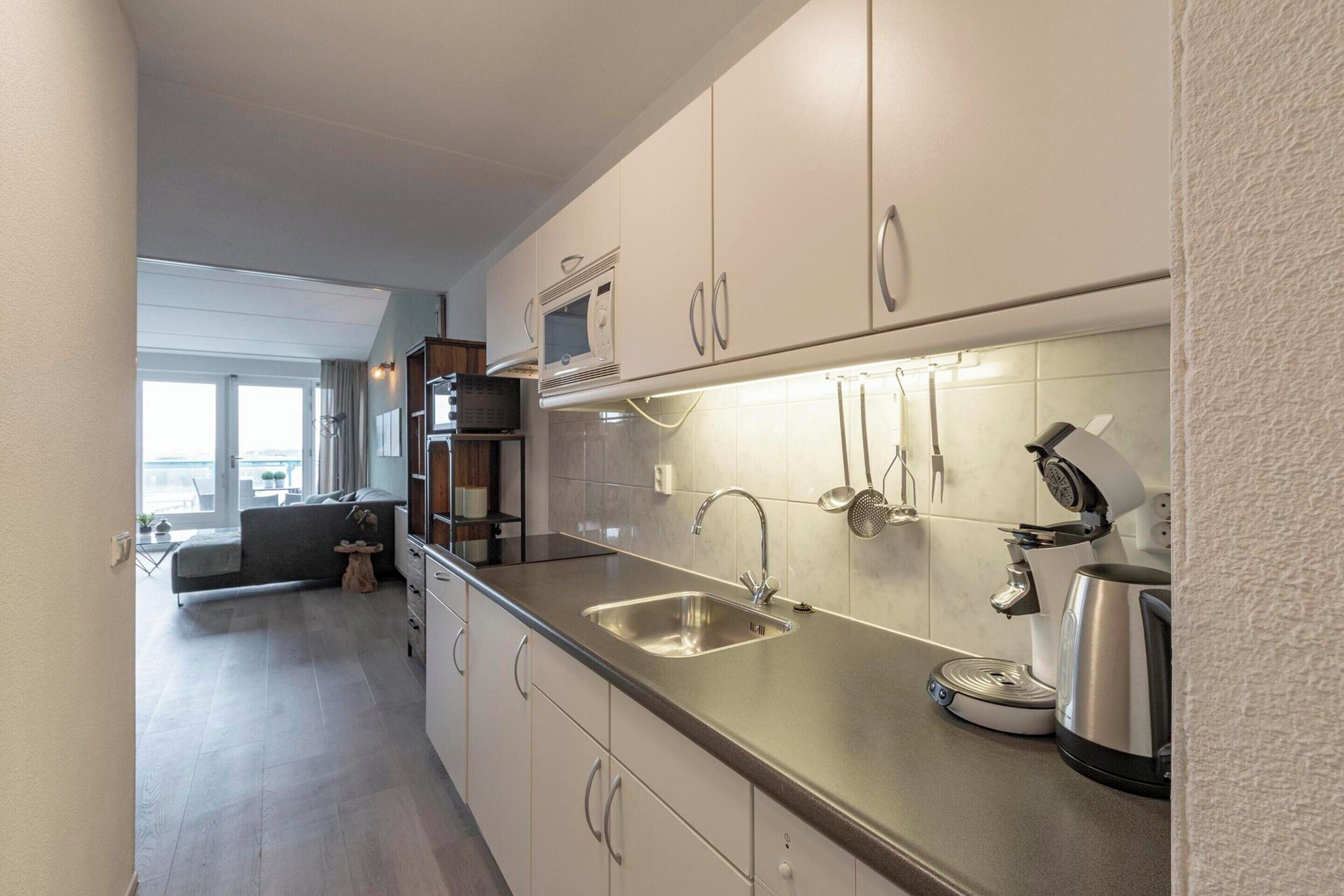 A modern kitchen with a stainless steel sink, a built-in microwave, and a coffee machine.