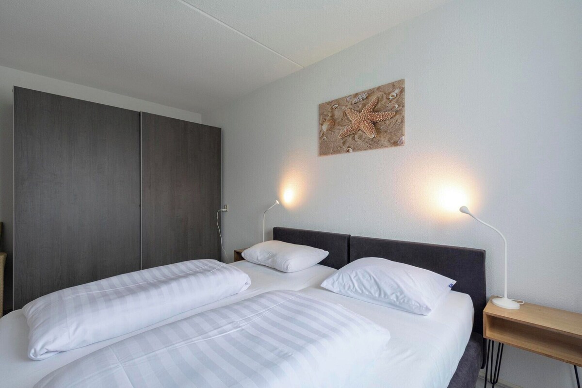Una cama doble con ropa de cama blanca, un cabecero oscuro, dos mesitas de noche con lámparas y una obra de arte colgada en la pared.