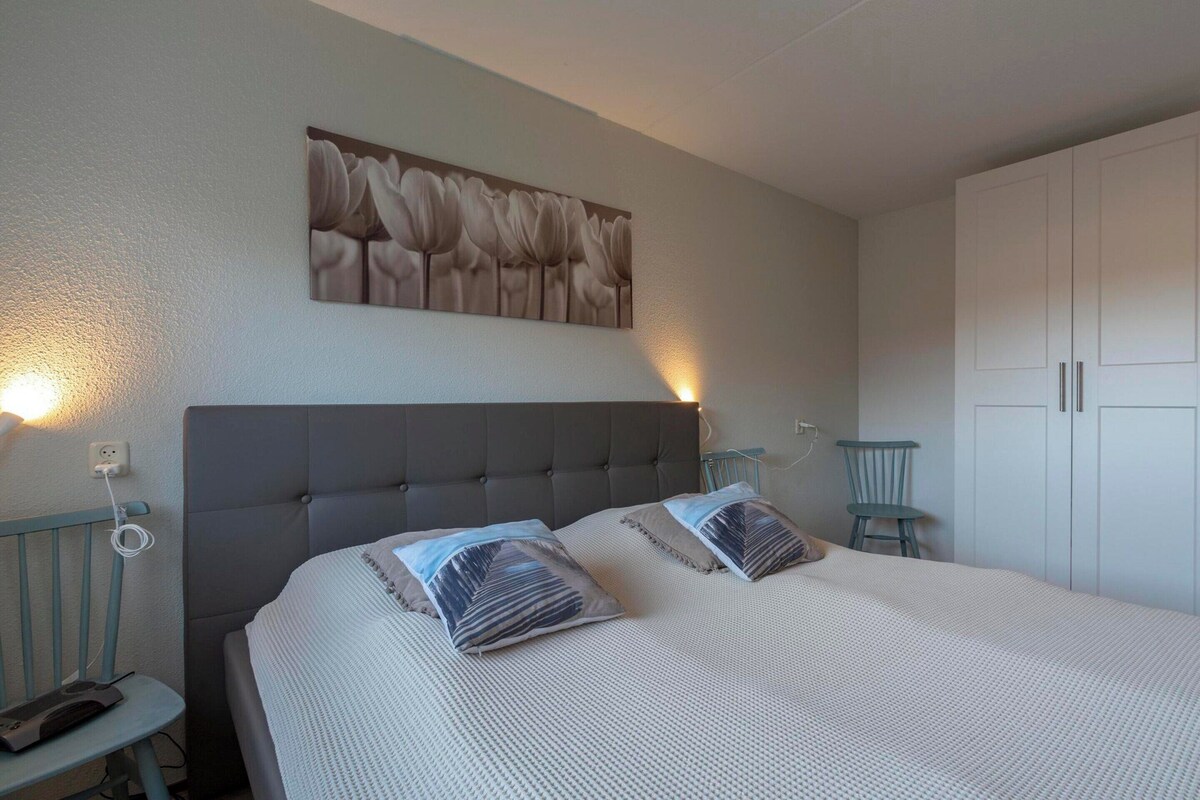 Un dormitorio con cama, dos mesitas de noche, una lámpara de pared, una silla y un armario.