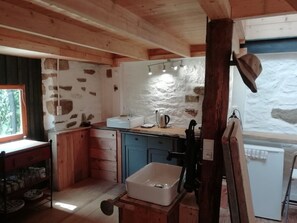 A rustic kitchen with exposed stone walls, wooden beams, a sink, and a window. - Brittany Escape With Garden (Cleden-Cap-Sizun)