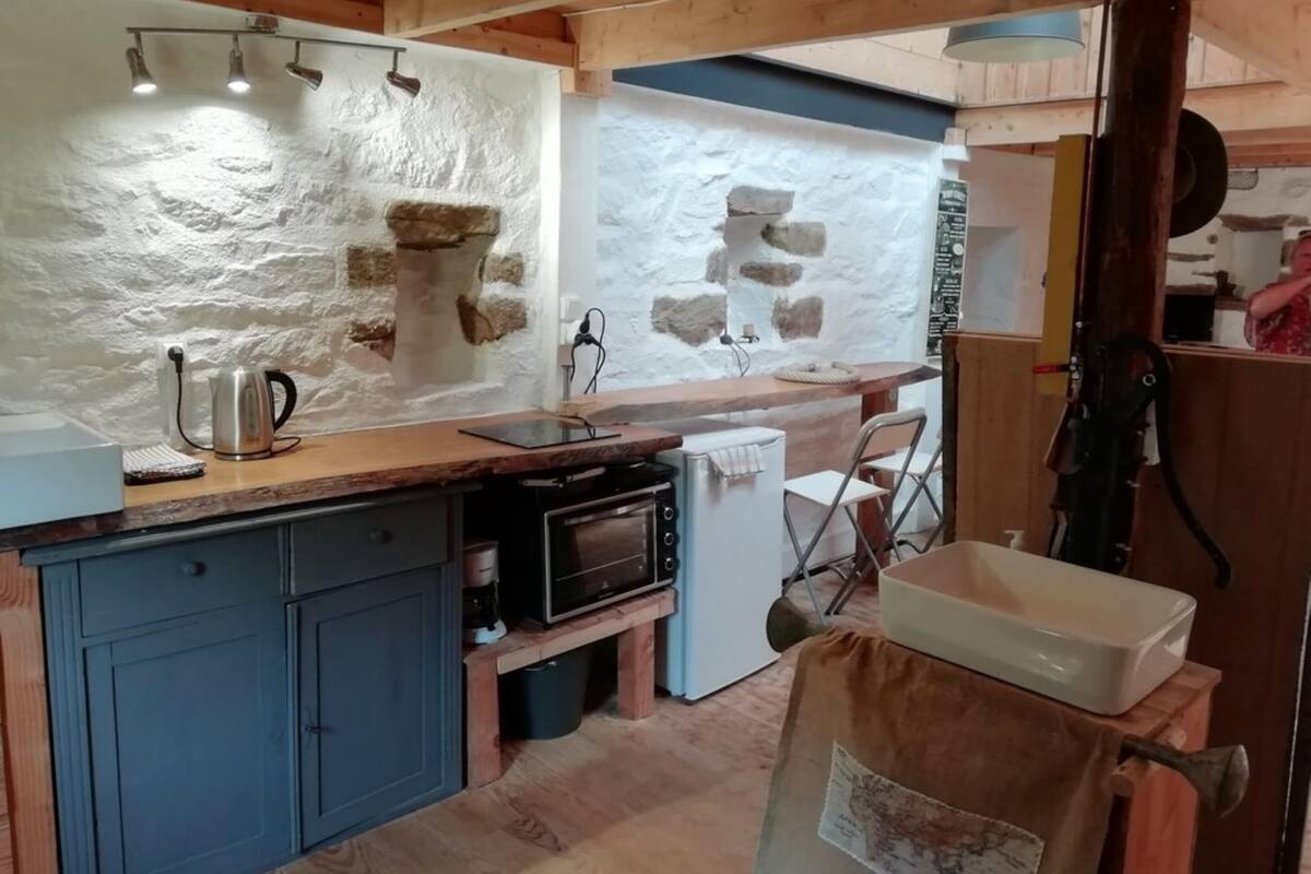 A rustic kitchen with stone walls, a wooden countertop, and a small refrigerator.