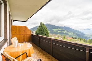 Ein Balkon mit Tisch und Stühlen, Holzverkleidung und Blick auf eine gebirgige Landschaft.