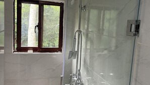 A glass-enclosed shower with a handheld showerhead, a window with a view of greenery, and a door with a handle. - Aromas de campo hotel (Inoa)
