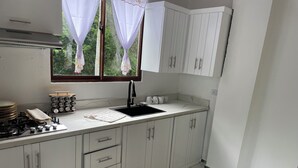 A kitchen with white cabinets, a gas stove, a sink, and a window with curtains. - Aromas de campo hotel (Inoa)