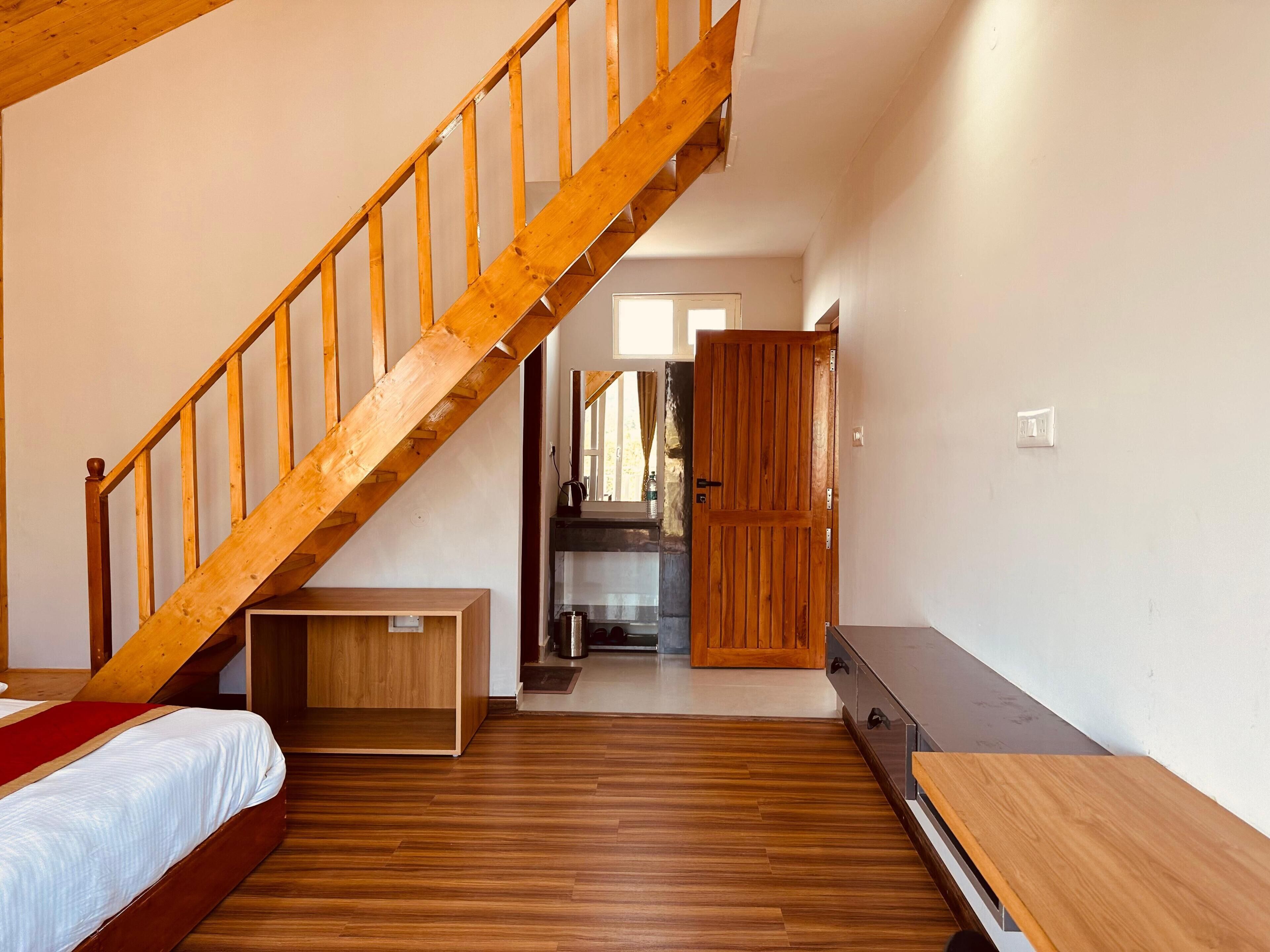 Une chambre avec un escalier en bois, un lit, un petit banc en bois et une armoire.