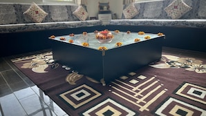 Une pièce avec une table basse dont le plateau est en verre, un tapis à motifs et une vue par la fenêtre.
