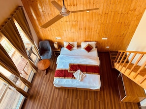 A room with a bed, a chair, a table, a ceiling fan, and a wooden floor. - The Billing Health Resort (Baijnath)