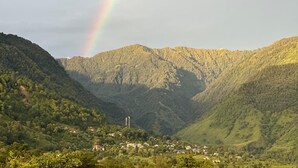 Un paysage montagneux avec un arc-en-ciel, de la végétation luxuriante et un petit village.