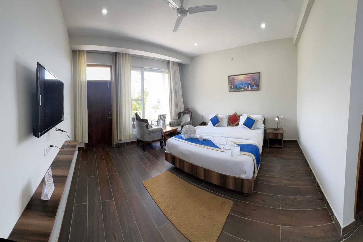 A hotel room with a bed, a desk, a chair, a television, and a painting on the wall.