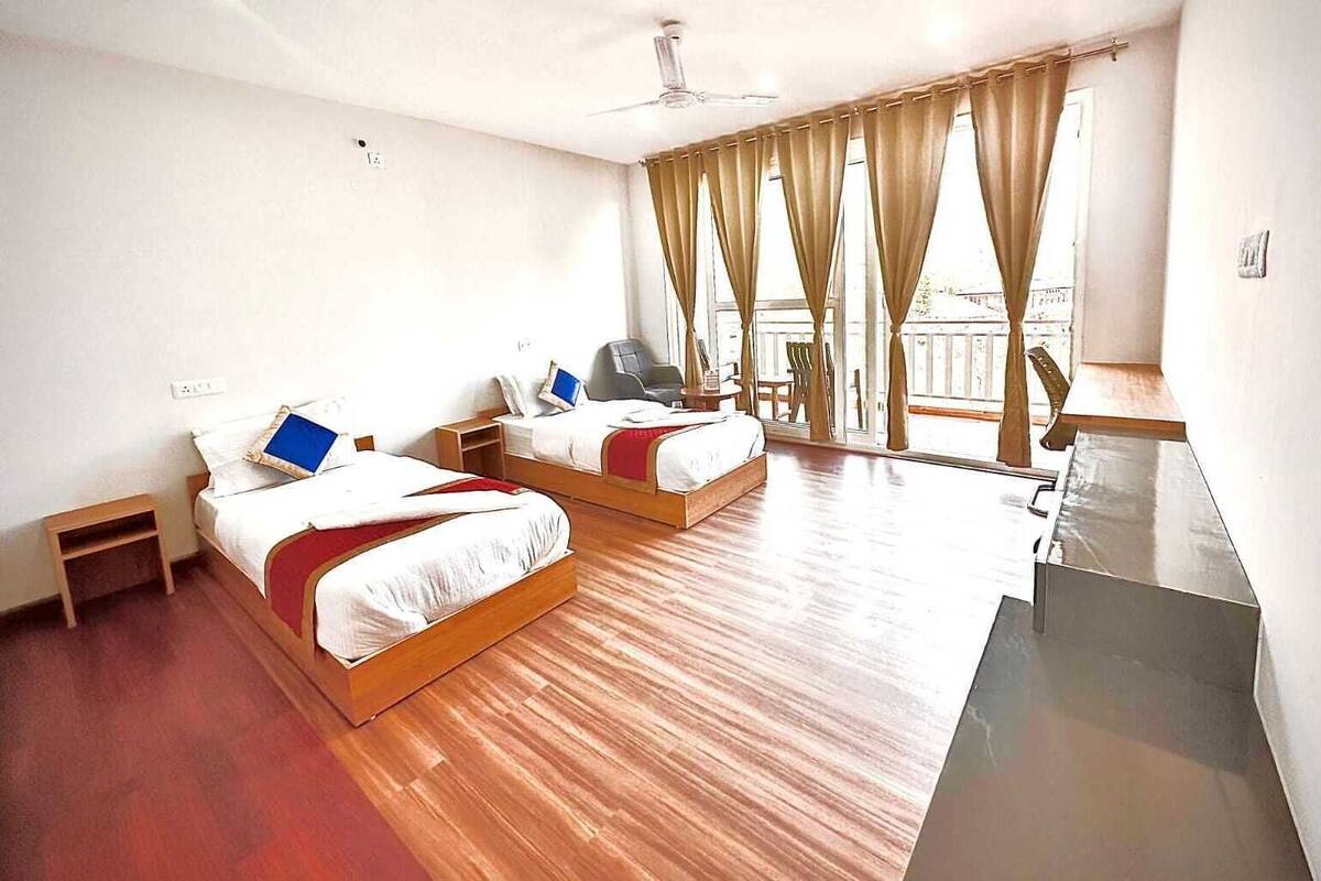 A hotel room with two beds, a desk, a chair, a laptop, and a balcony with curtains.