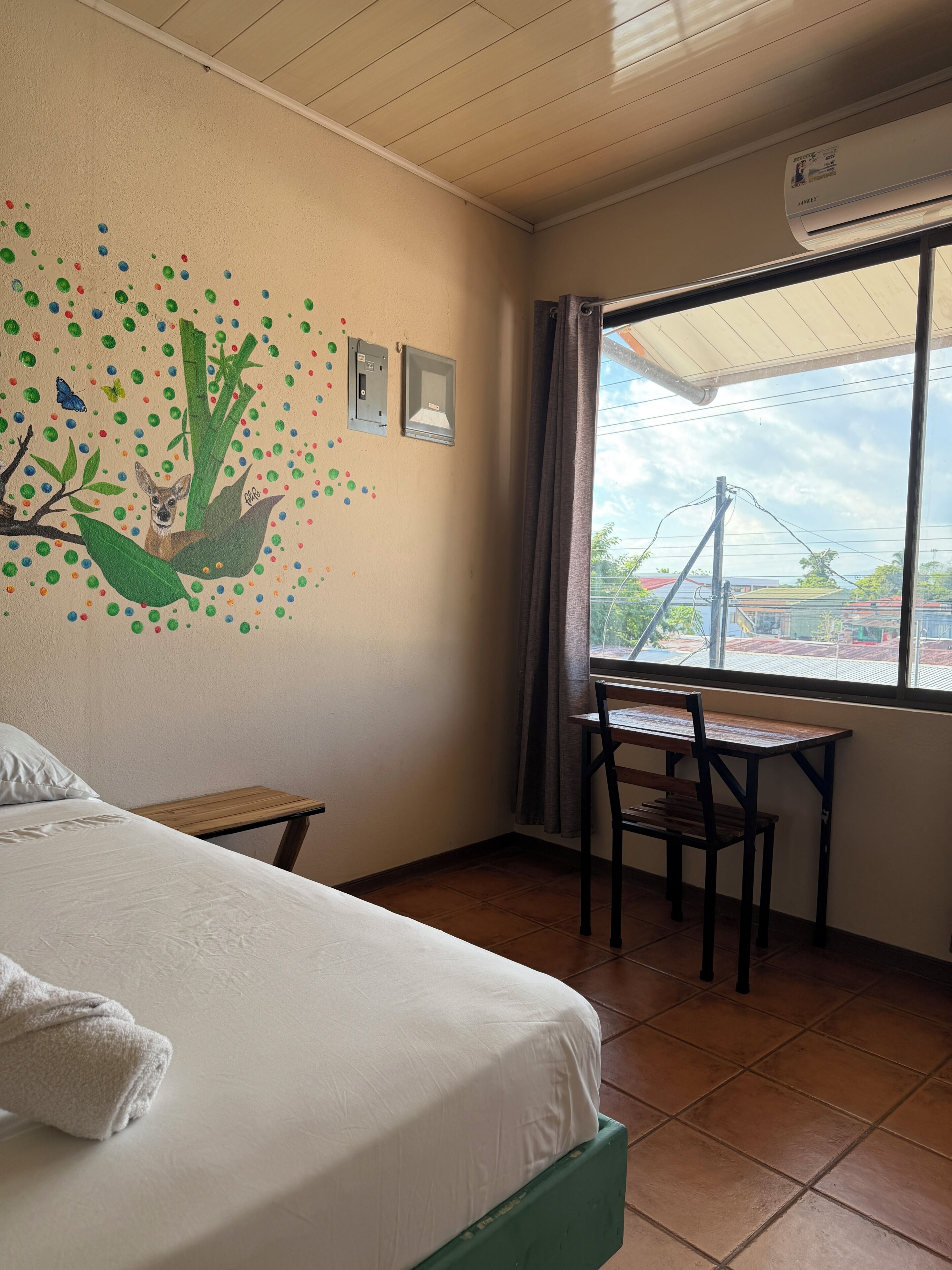 Ein Hotelzimmer mit Bett, Schreibtisch, Stuhl, Fenster mit Aussicht und einer Wand mit Wandgemälde.
