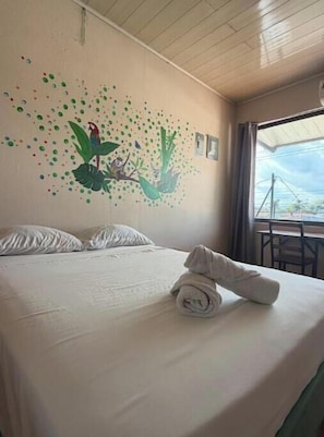 A hotel room with a bed, a wall mural, and a window.