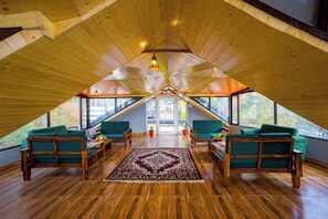A spacious attic room with wooden floors, green upholstered sofas, and a large window providing a view of the outdoors.