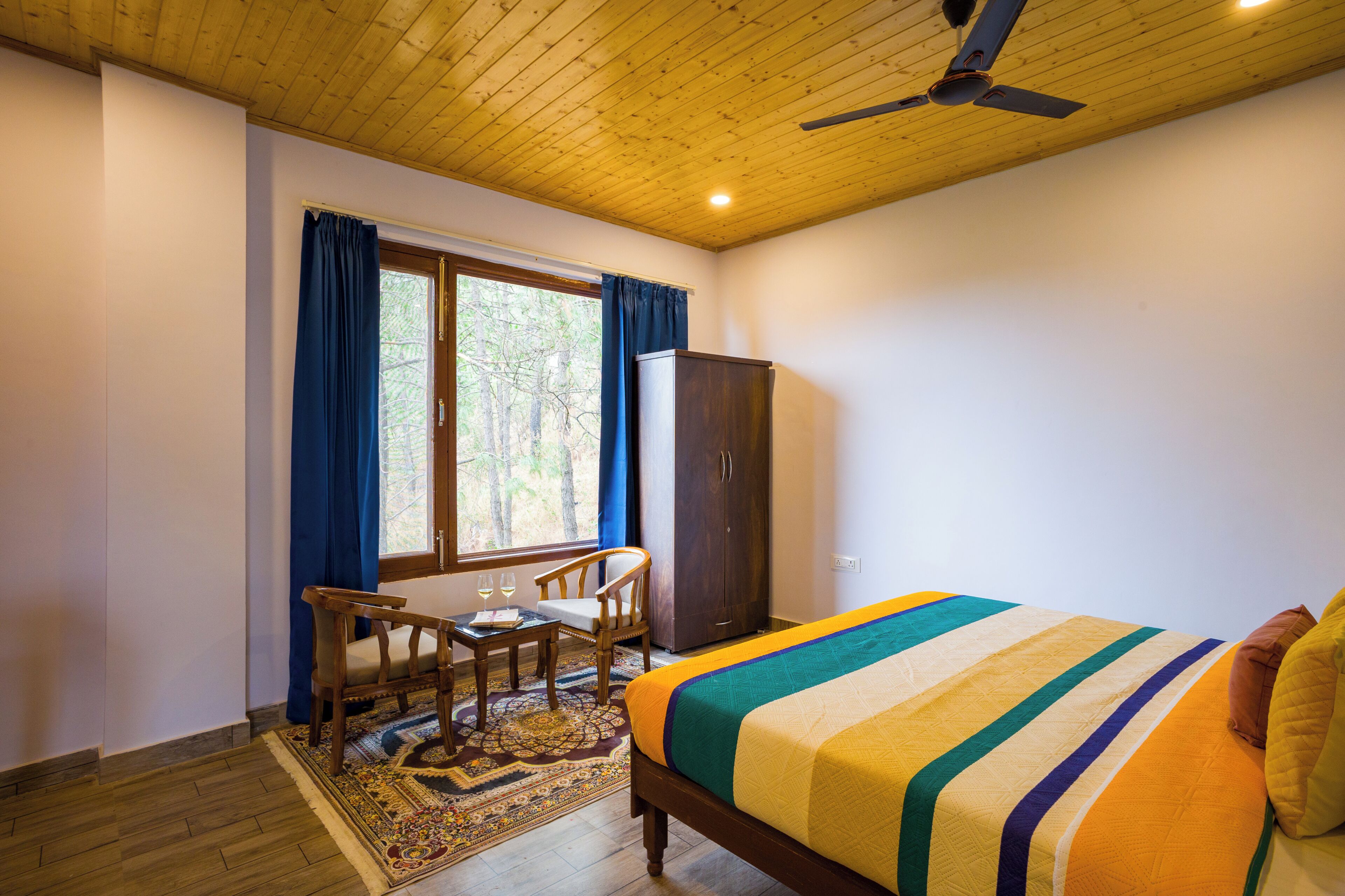 Une chambre à coucher comprenant un lit, un bureau avec deux chaises, une armoire et un ventilateur de plafond.