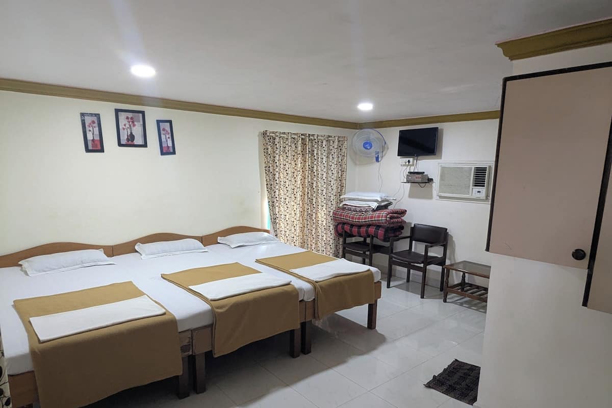 Habitación de hotel con tres camas, un escritorio, una silla, un televisor y un ventilador.
