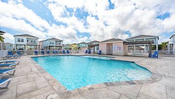 A swimming pool with lounge chairs, a covered area, and colorful buildings in the background.
