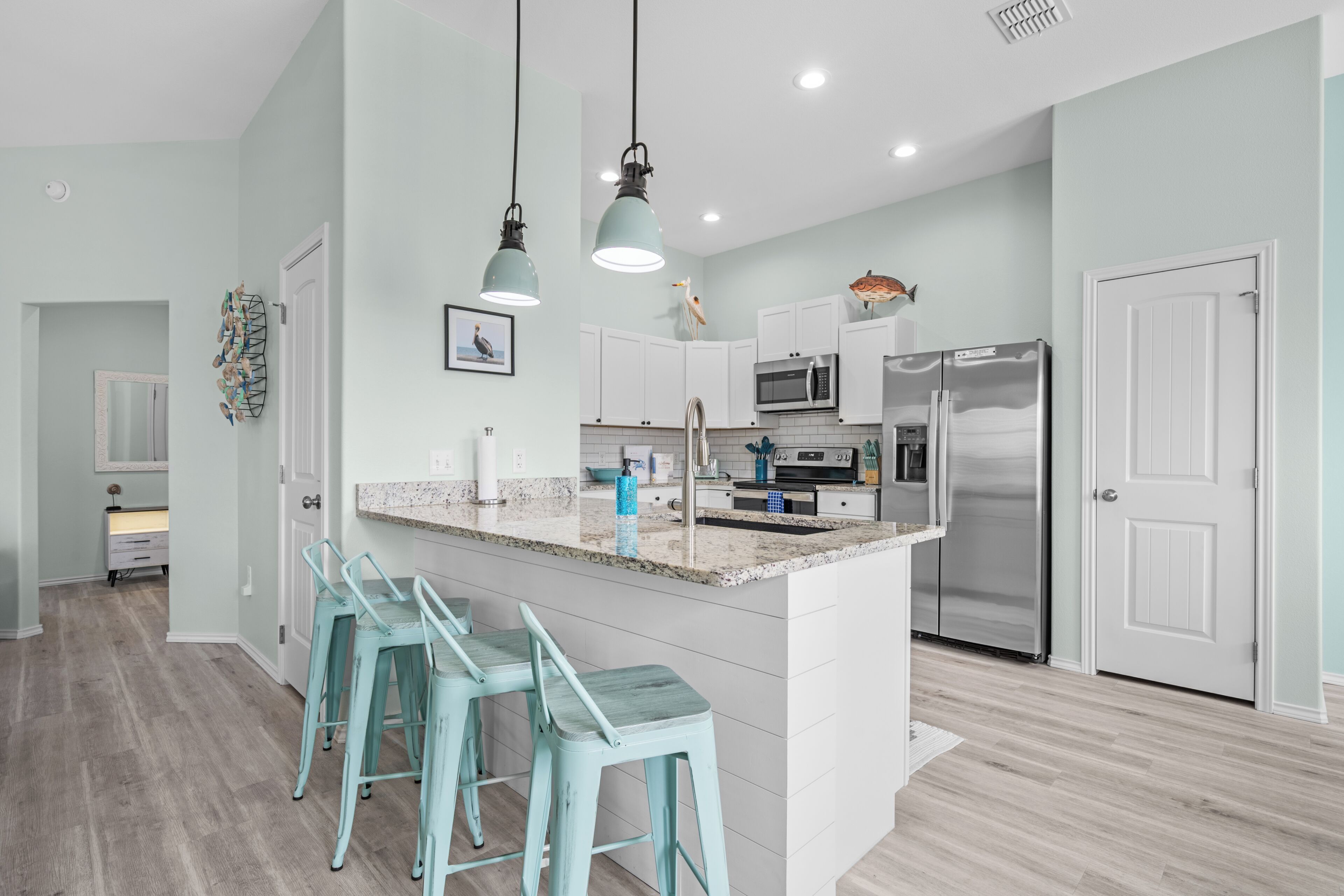 A modern kitchen with white cabinets, stainless steel appliances, and teal bar stools.