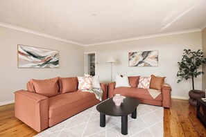 A living room with two sofas, a coffee table, and artwork on the walls. - 4BR Arncliffe Hidden Gem | Bungalow with Pool+BBQ (Arncliffe)