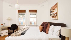 Een slaapkamer met een bed, een bureau, een stoel en een raam met jaloezieën.