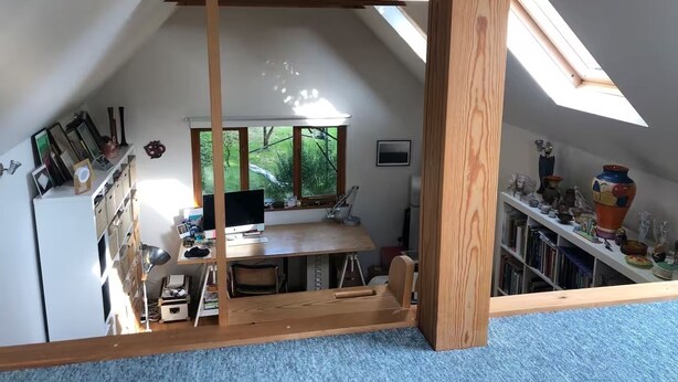 Une pièce de style « loft », avec un plafond en pente, un bureau avec un ordinateur, une bibliothèque et une grande fenêtre.