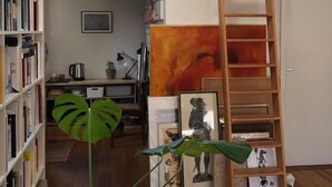 Une pièce de style loft avec une échelle en bois, une bibliothèque, un grand tableau et une plante.