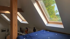 Une pièce avec un plafond en pente, des fenêtres de toit, un lit et une étagère contenant divers objets.