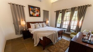 A bedroom with a bed, two bedside tables, a desk, a chair, a rug, and curtains. - ELIVAAS Casa Mocha Exquisite 5BHK Villa (Alibag)