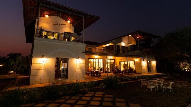 A two-story house with a balcony, outdoor seating area, and a well-lit entrance. - ELIVAAS Casa Mocha Exquisite 5BHK Villa (Alibag)