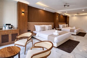 A hotel room with a large bed, two bedside tables, a coffee station, two wicker chairs, and a marble floor.