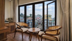 A balcony with two wicker chairs, a small table, and a view of buildings through large windows. - Valmere Chery Blossom Suites (Shillong)