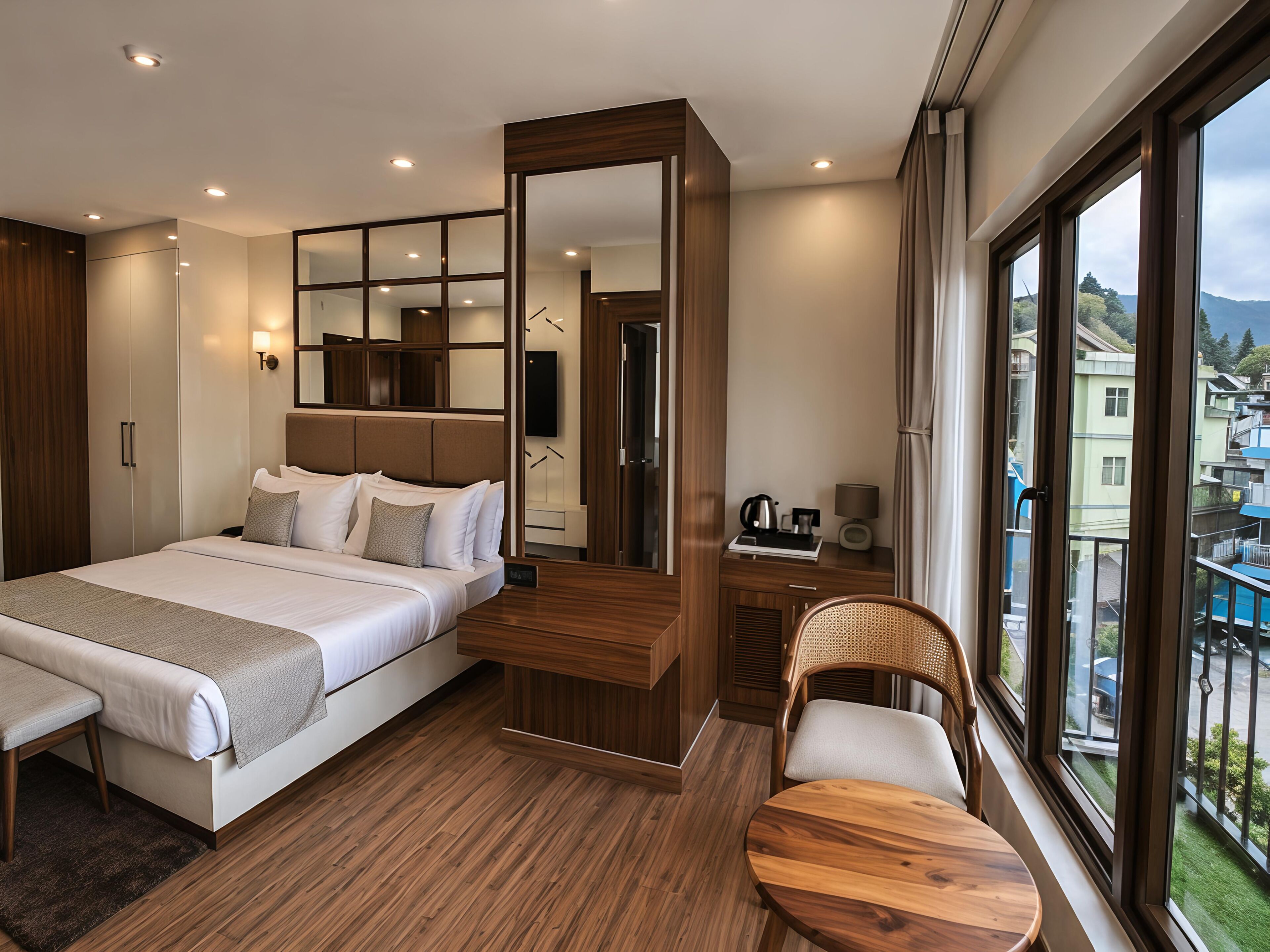 Quarto de hotel moderno com uma cama grande, uma escrivaninha de madeira, uma cadeira, uma TV e uma varanda com vista para edifícios e colinas.