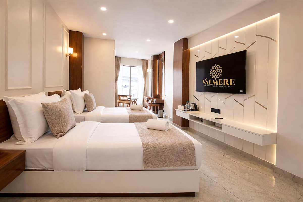 A modern hotel room with two beds, a TV, and a dining area.