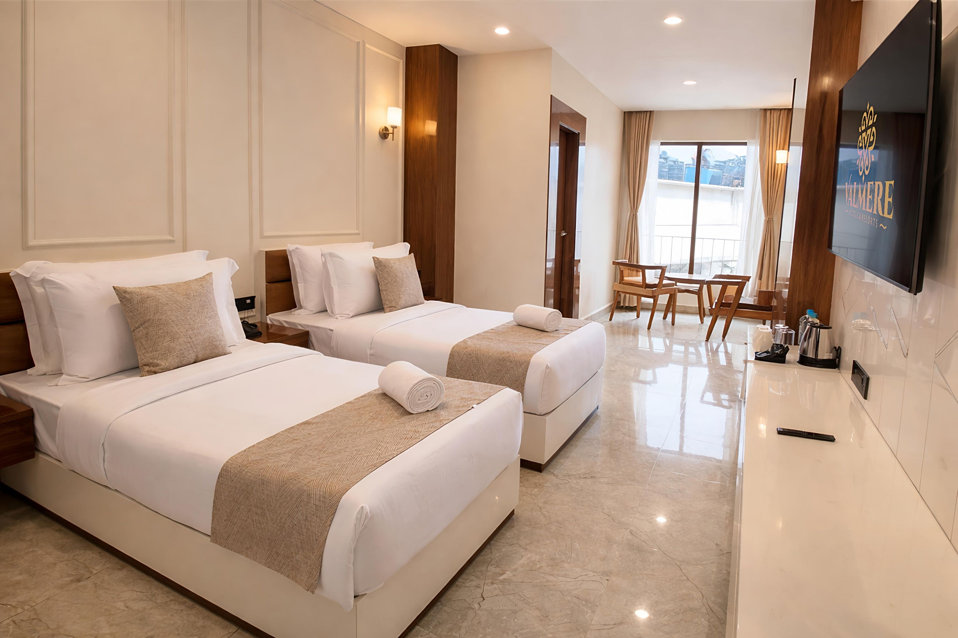 A hotel room with two beds, a TV, a dining area, and a balcony with a view.