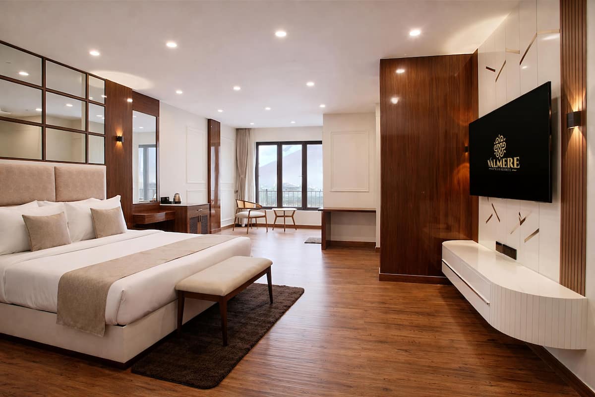 A modern hotel room with a large bed, a desk, a TV, and a view of the city.