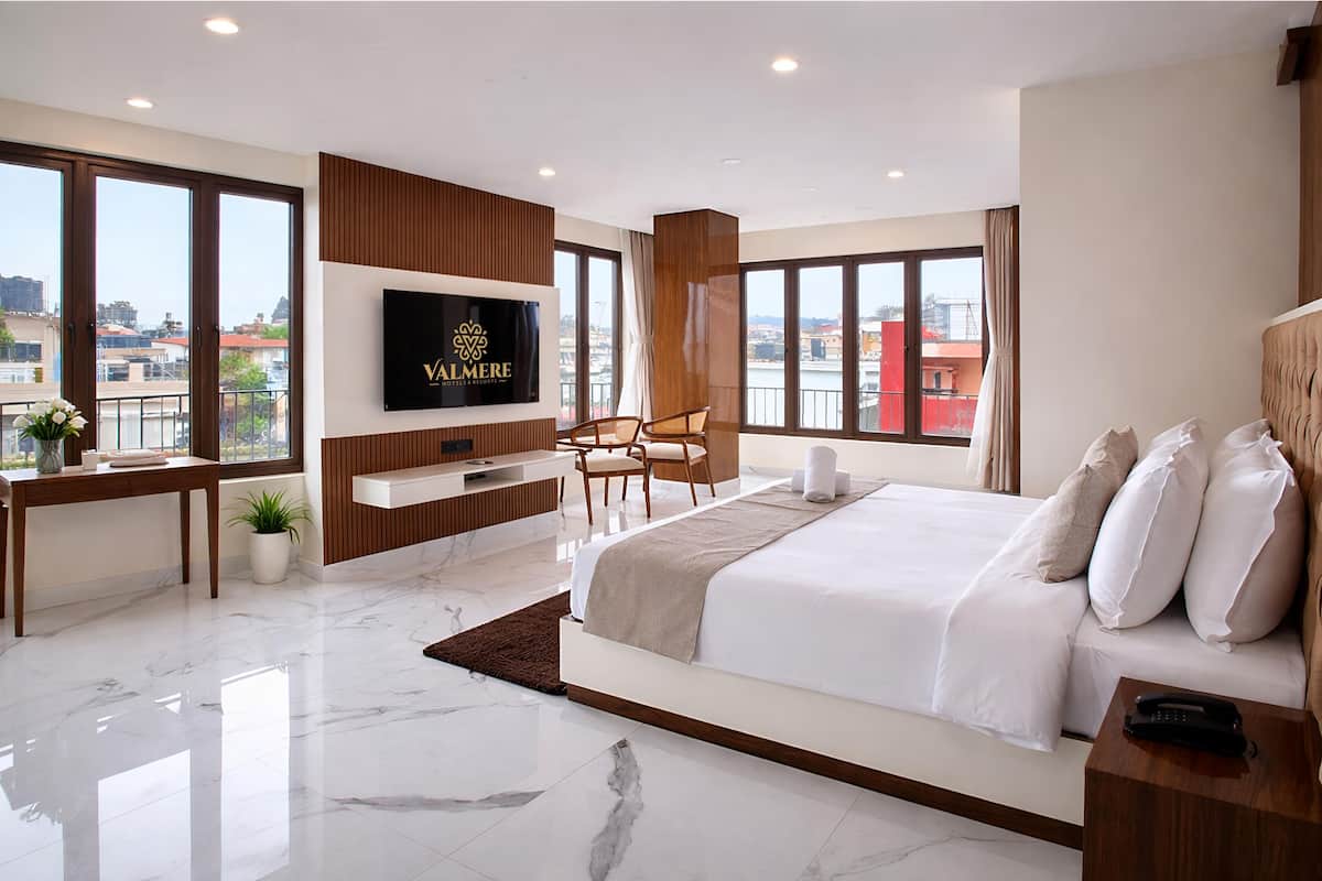 A modern hotel room with a large bed, a TV mounted on the wall, a desk with a chair, and a view of the city.