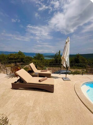Ein Poolbereich mit Liegestühlen und Sonnenschirm, mit Blick auf eine schöne Landschaft.
