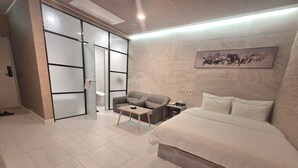 A modern hotel room with a bed, a sofa, a small table, and a nightstand. - Suwon Station Hotel Terry's (Suwon)