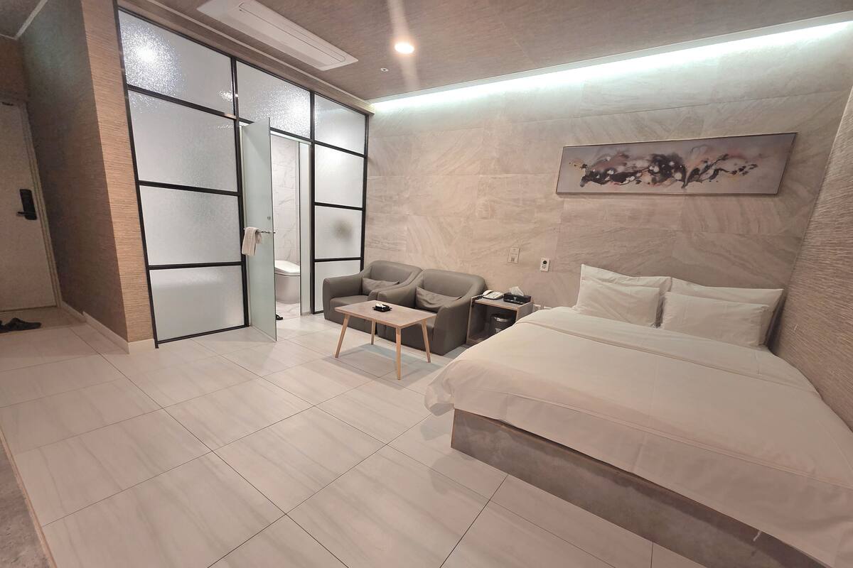Habitació d'hotel moderna amb un llit, un sofà, una taula petita i una tauleta de nit.